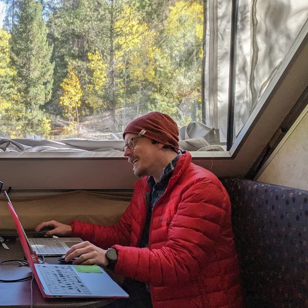 Ryan Haack working from a camper surrounded by autumn trees